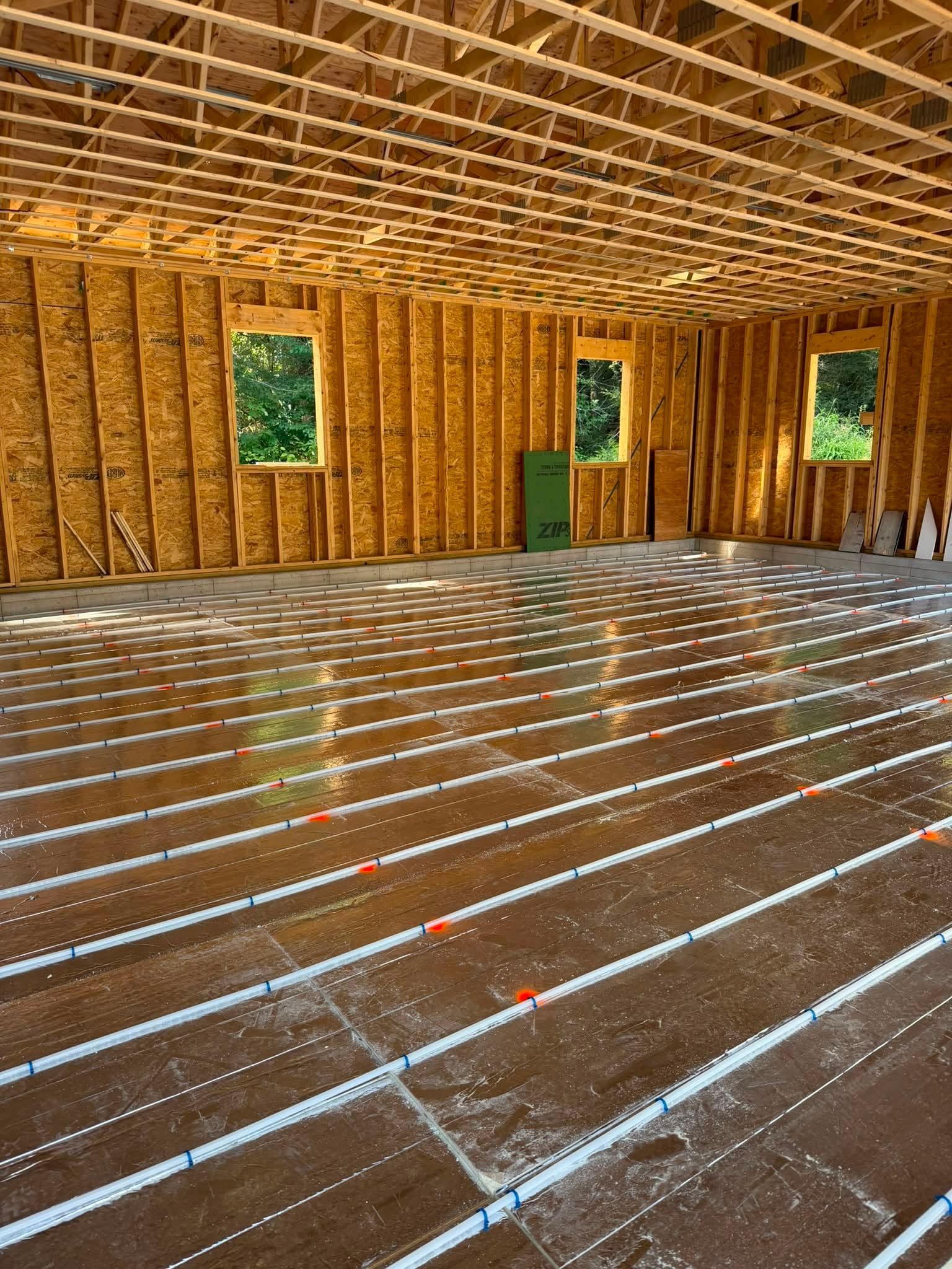 Wood-framed interior under construction with exposed insulation, windows, and a reflective unfinished floor