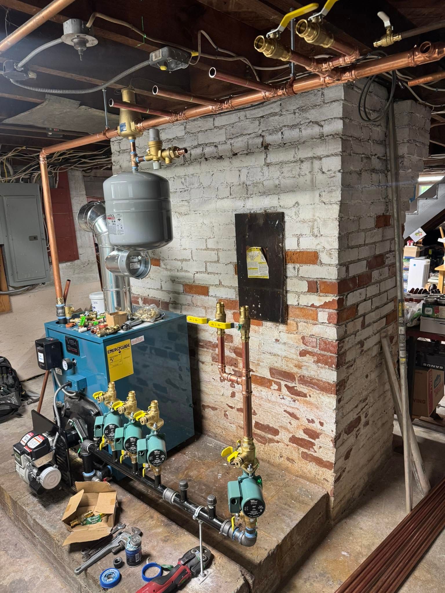 Basement utility room with exposed pipes, water heater, boiler, and masonry walls.