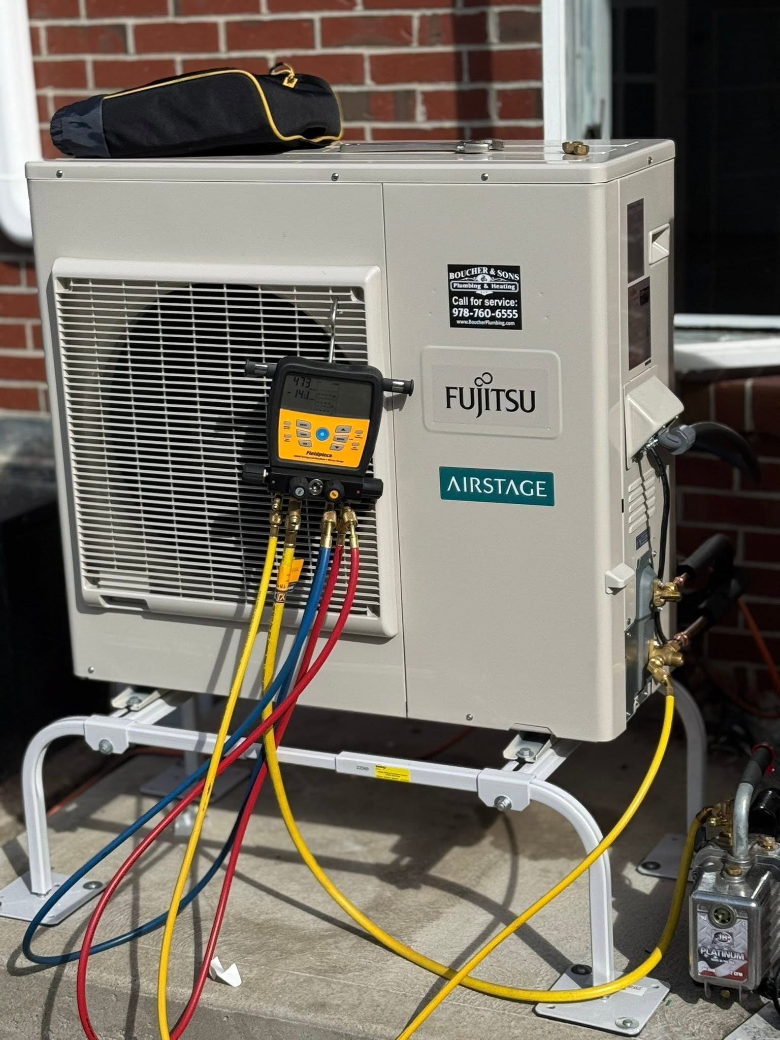Outdoor Fujitsu HVAC unit with attached gauges and colorful service hoses on concrete pad