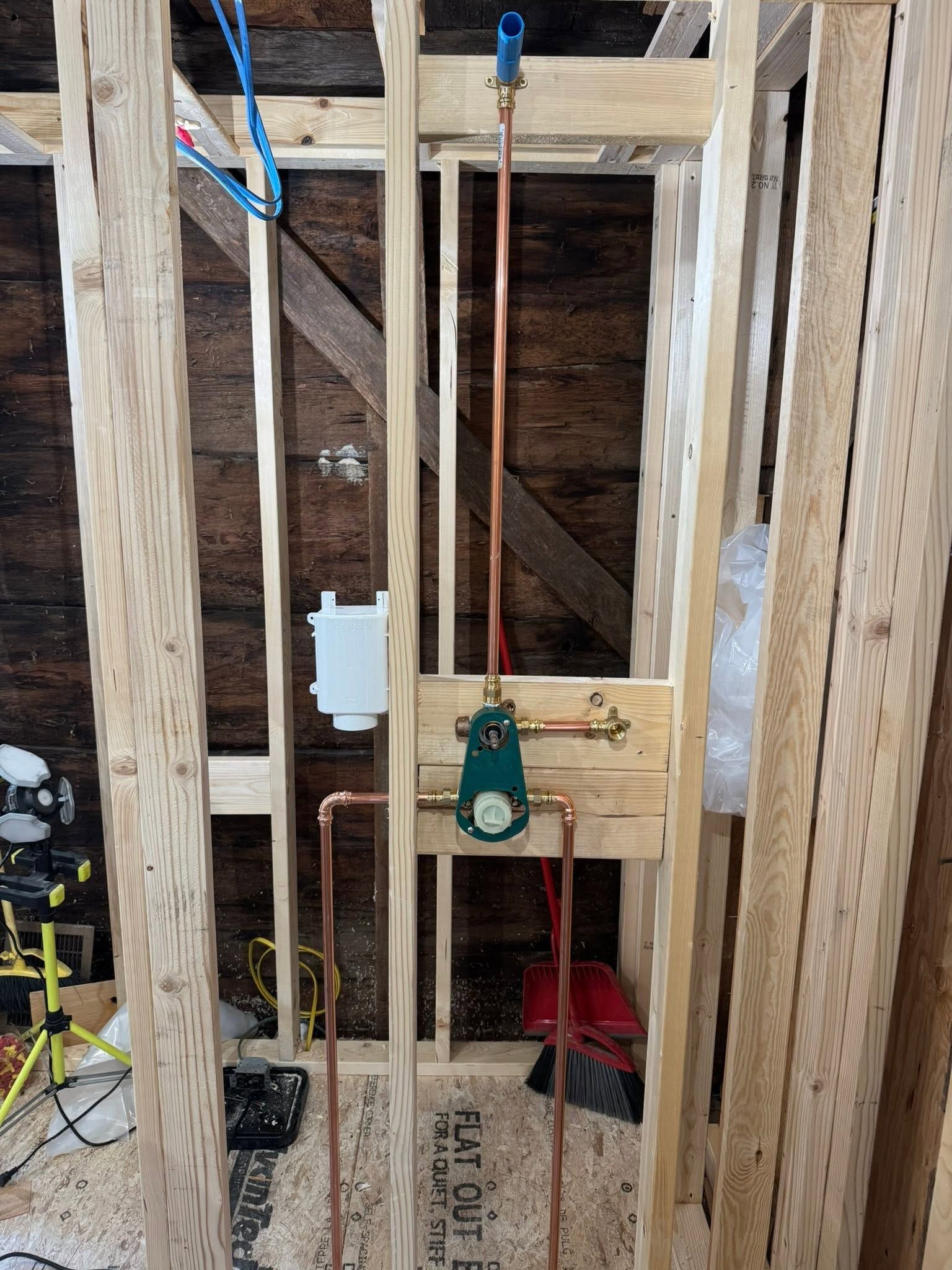 Framed wall with copper plumbing and a green valve assembly inside a construction area