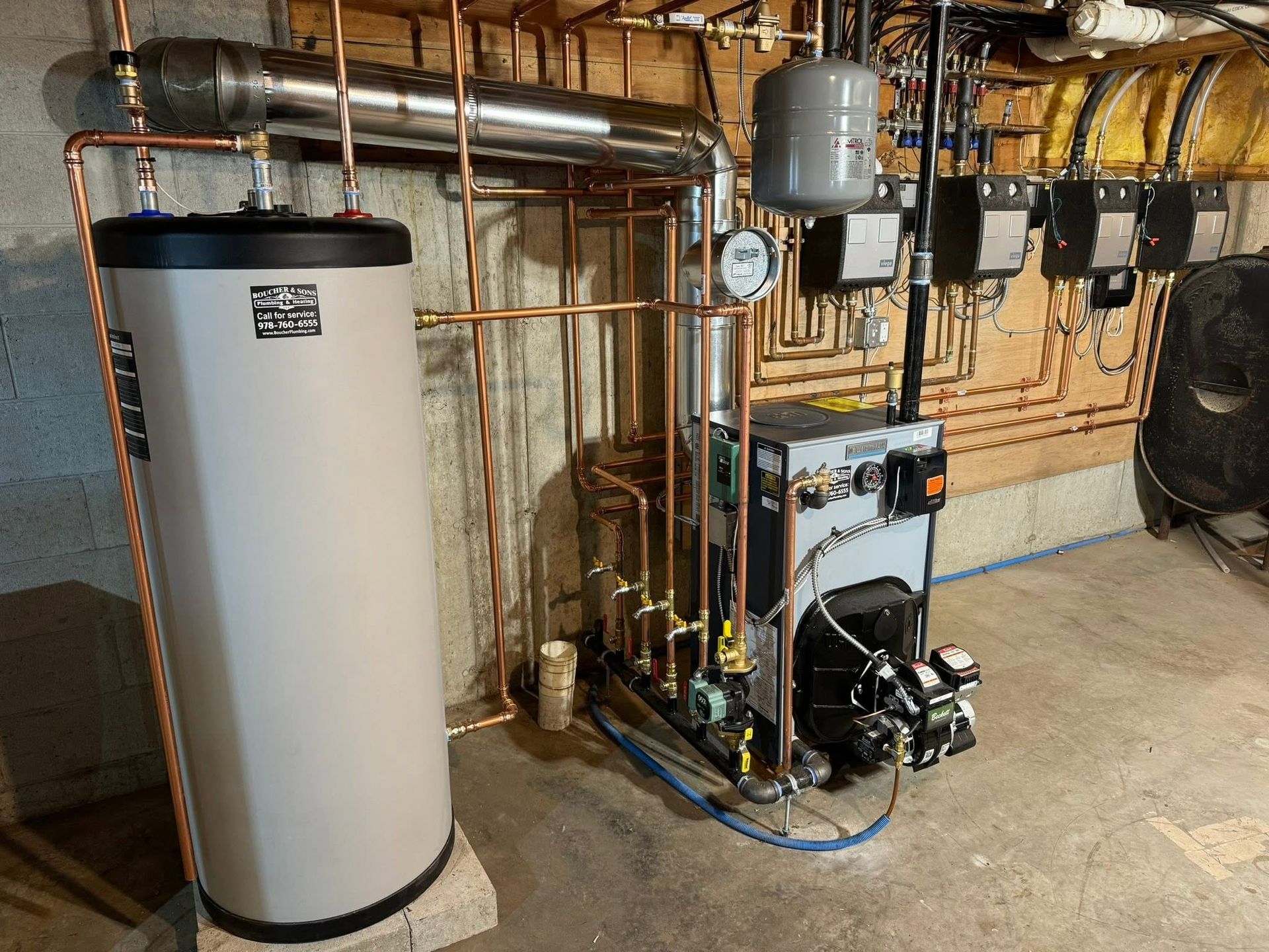 Basement utility room with a water heater, boiler, pipes, and gauges along the wall.