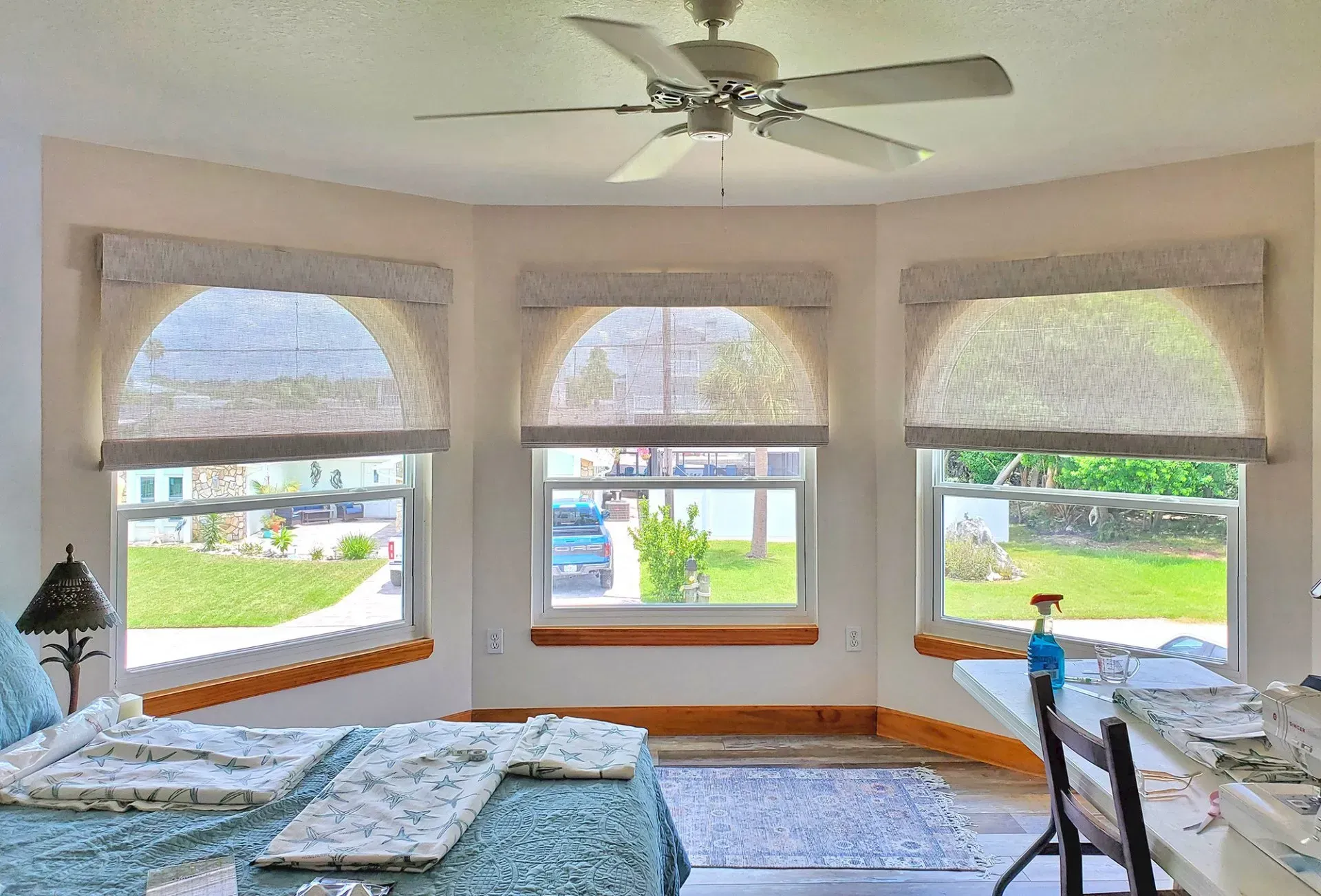 A room with arched windows, light-colored blinds, a ceiling fan, and a bed with blue bedding.