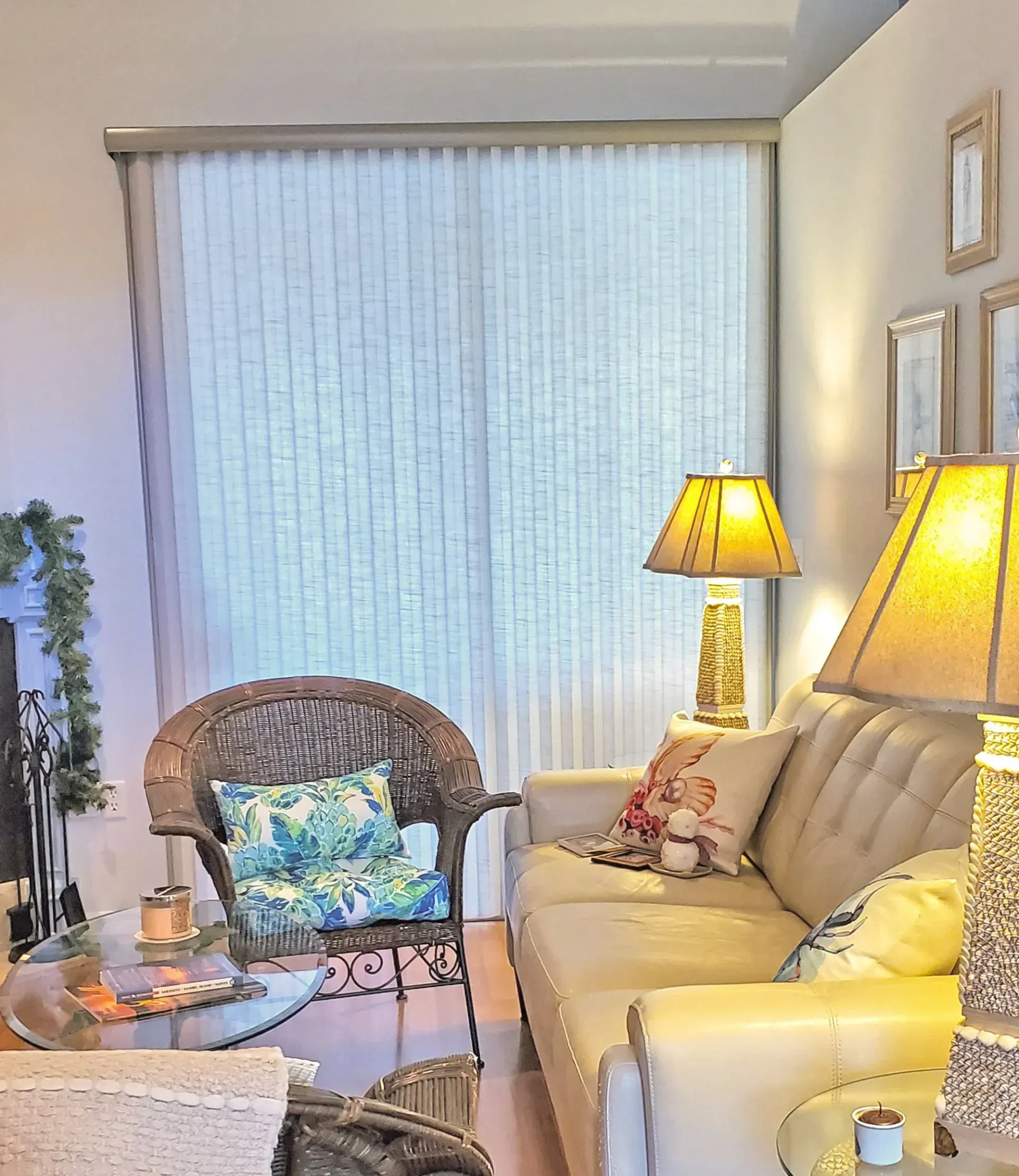 Cozy living room with wicker furniture, beige sofa, lamps with warm light, and light filtering window blinds.