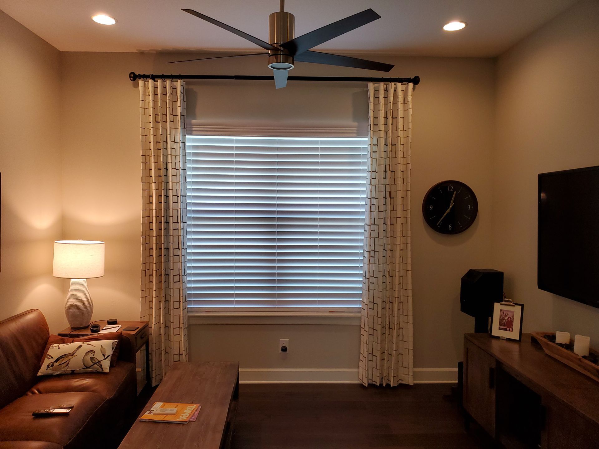 Living room with closed blinds, curtains, ceiling fan, sofa, TV, and side table.