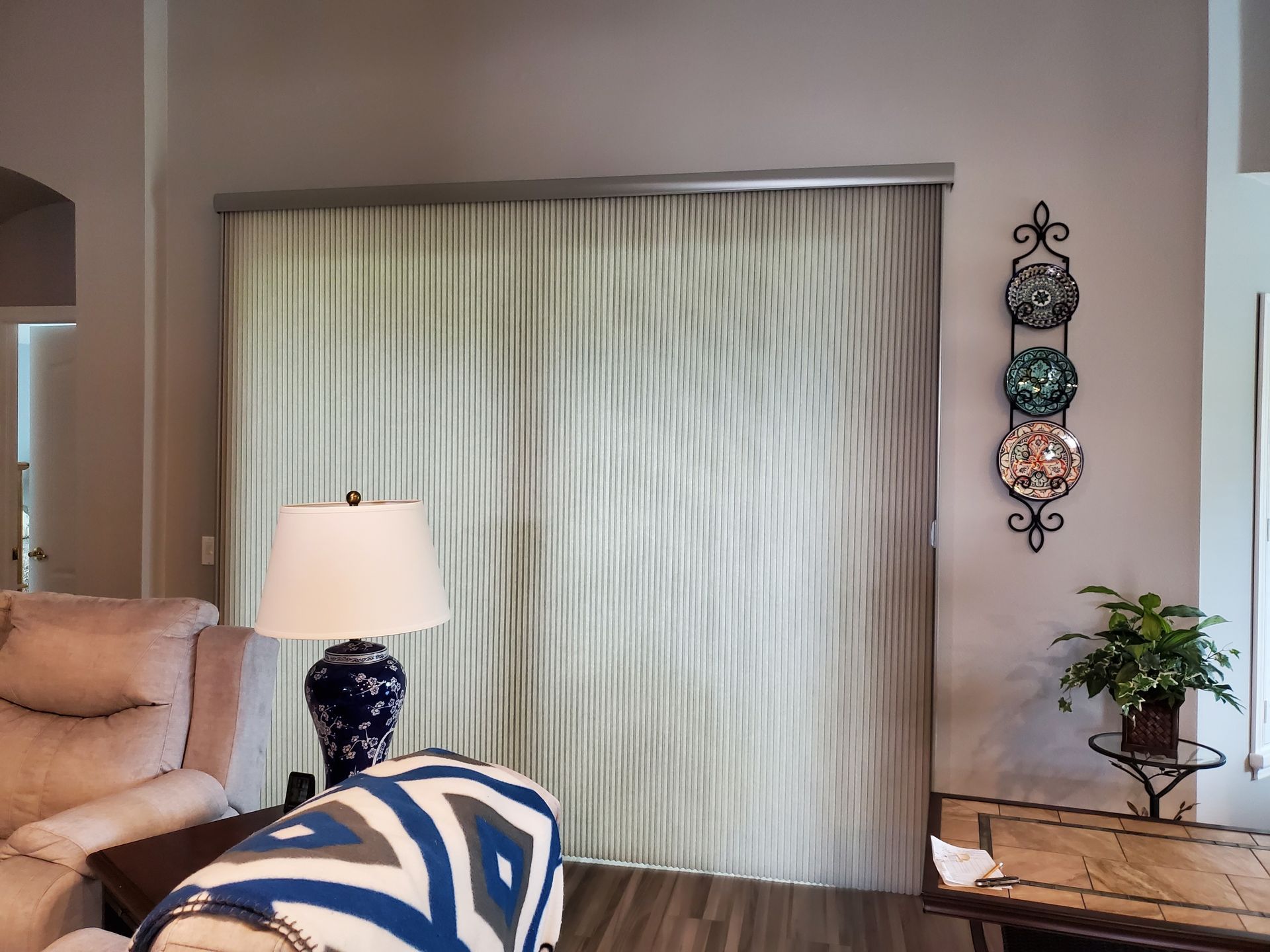 Living room with tall, light-colored curtains, a lamp, recliner, and decorative plates on the wall.