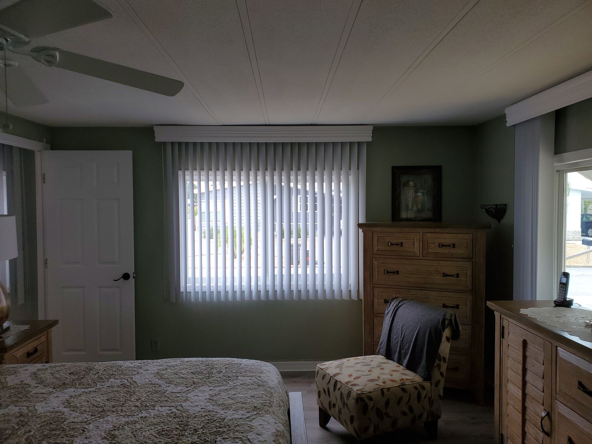Bedroom with bed, dresser, chair, and vertical blinds on a window. Green walls.