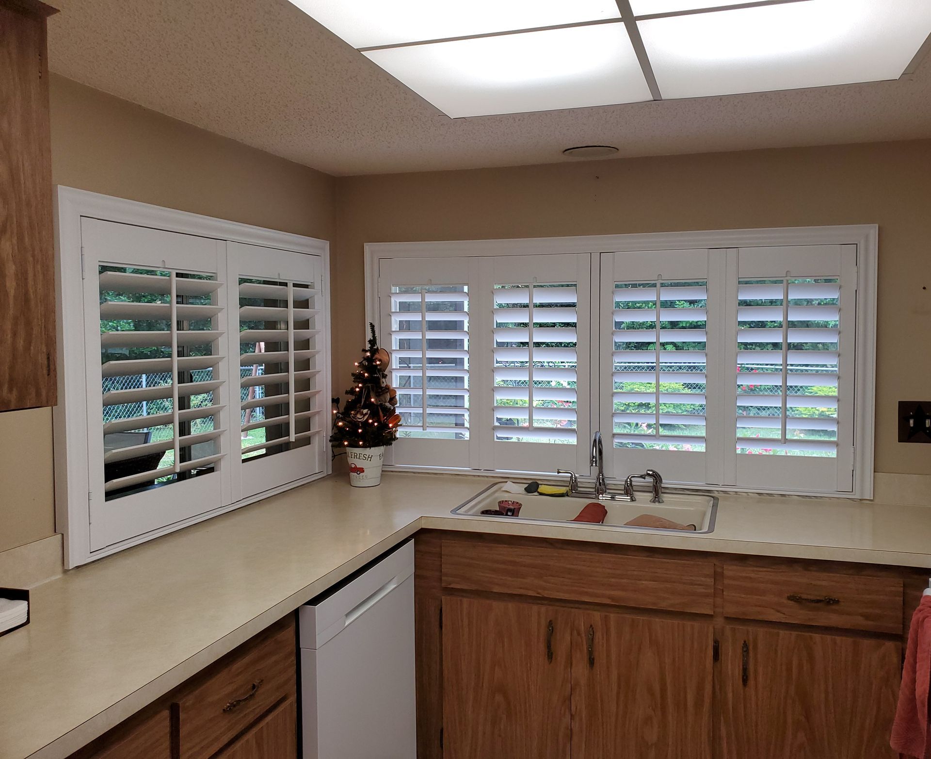 Kitchen with light countertops, white shutters, and wooden cabinets.