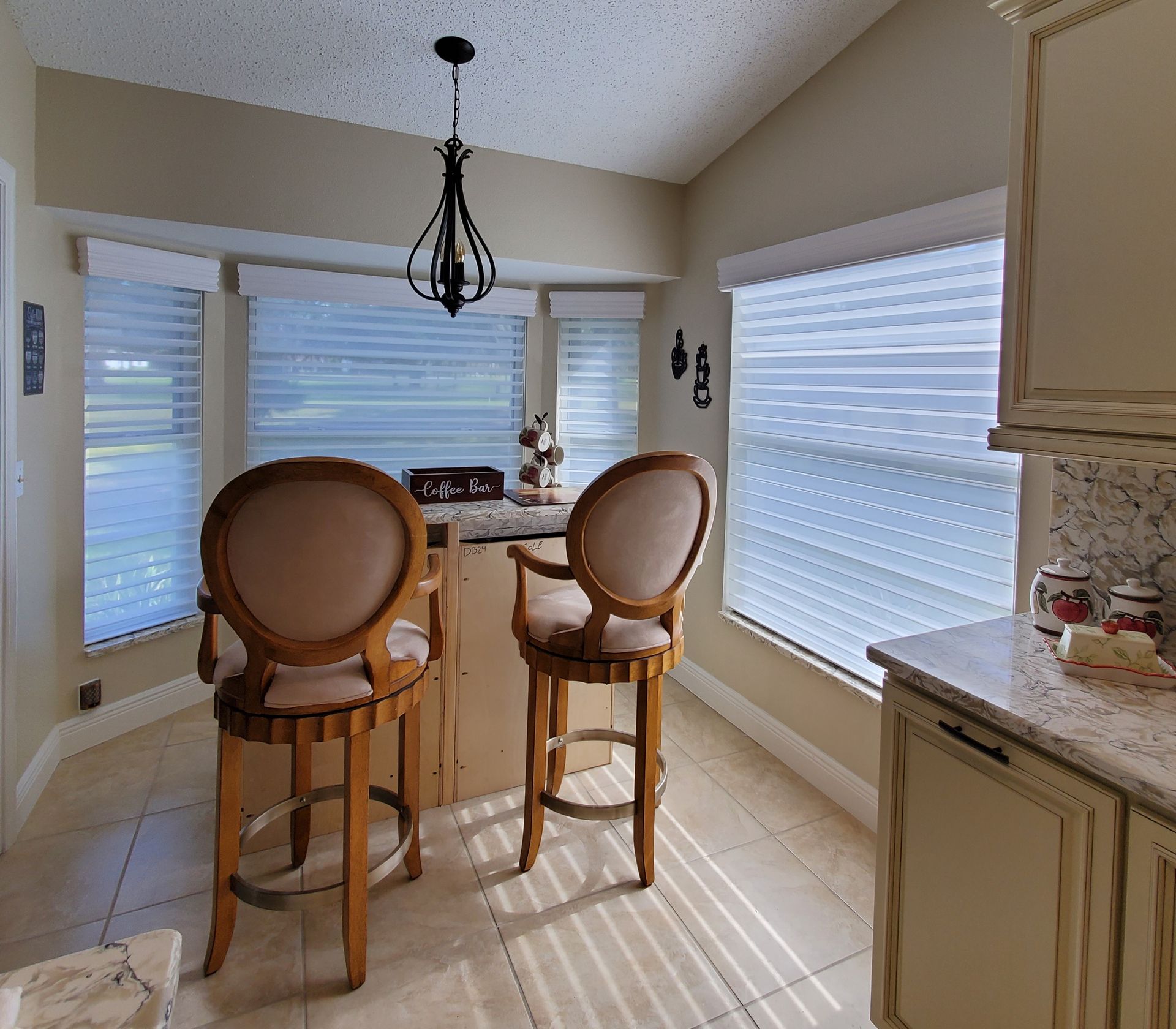 Kitchen with a breakfast bar, two stools, and a chandelier; window with blinds.