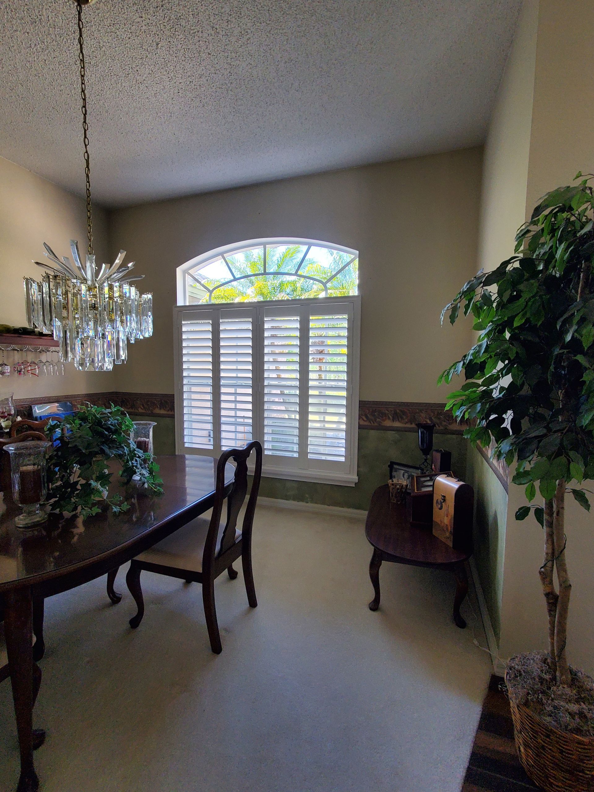 Dining room with chandelier, table, chairs, window with shutters, and plant.
