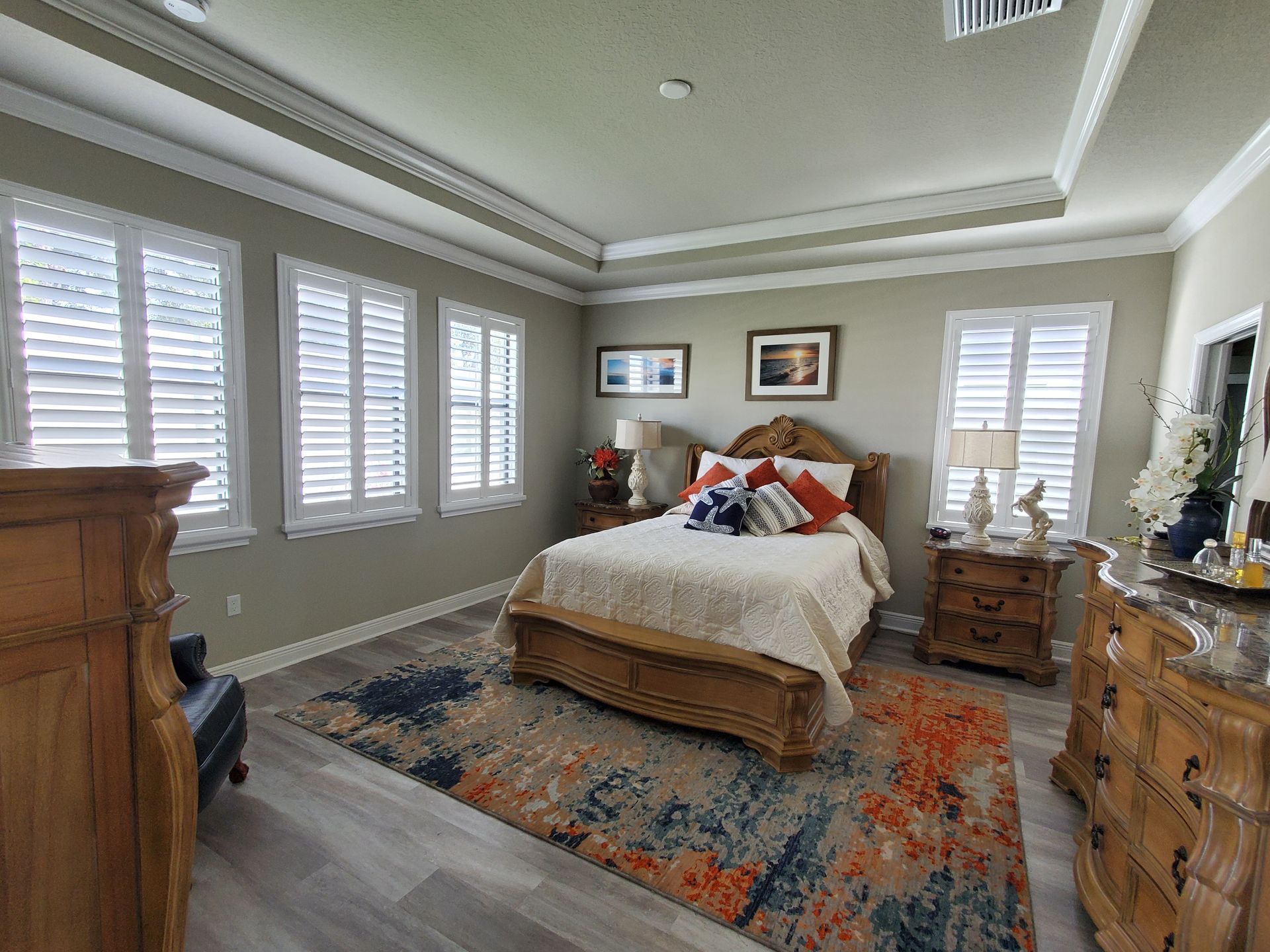 Bedroom with bed, windows with shutters, and wood furniture. Colorful rug and neutral walls.