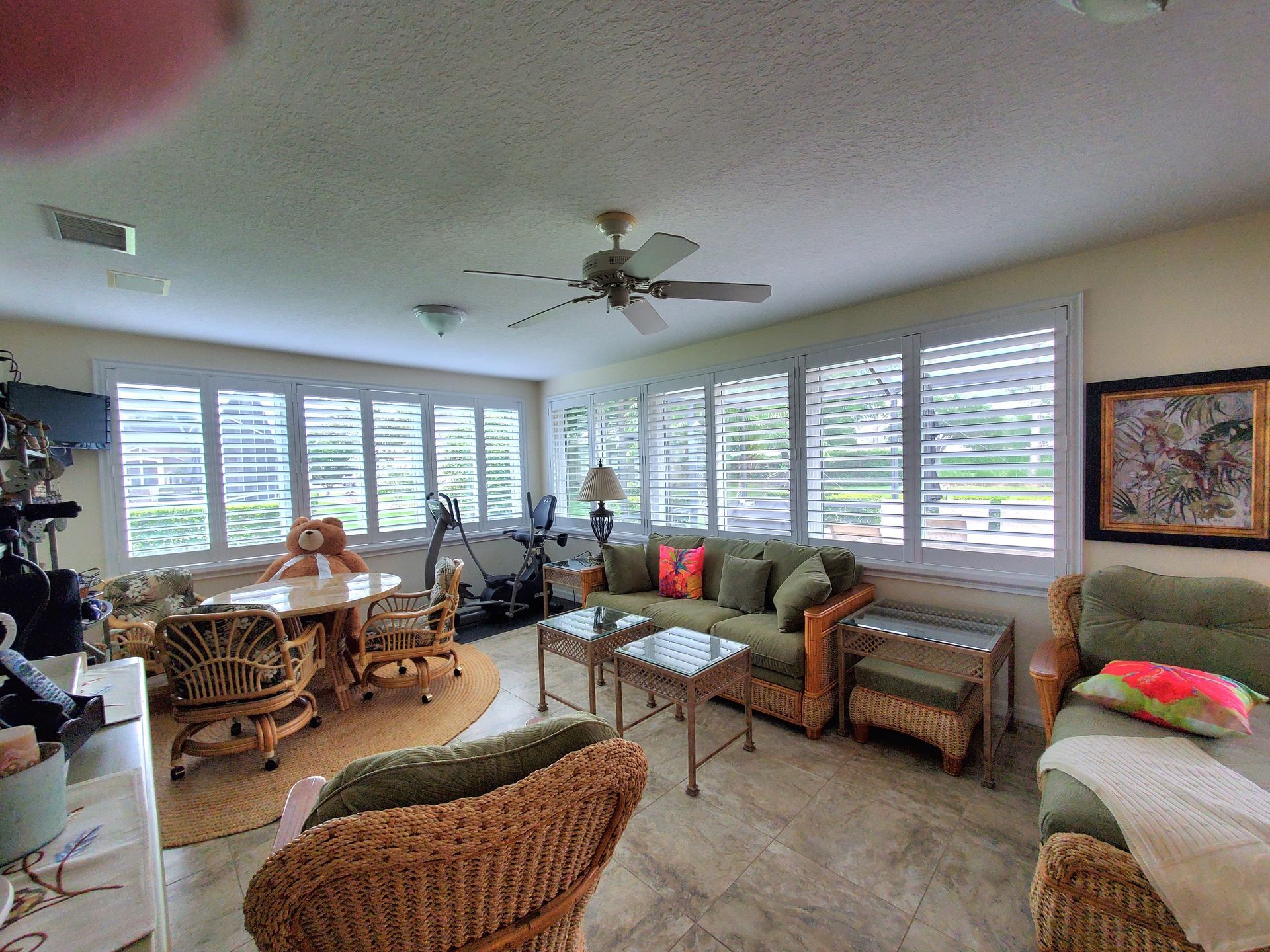 Sunroom with windows, shutters, wicker furniture, and a sofa.