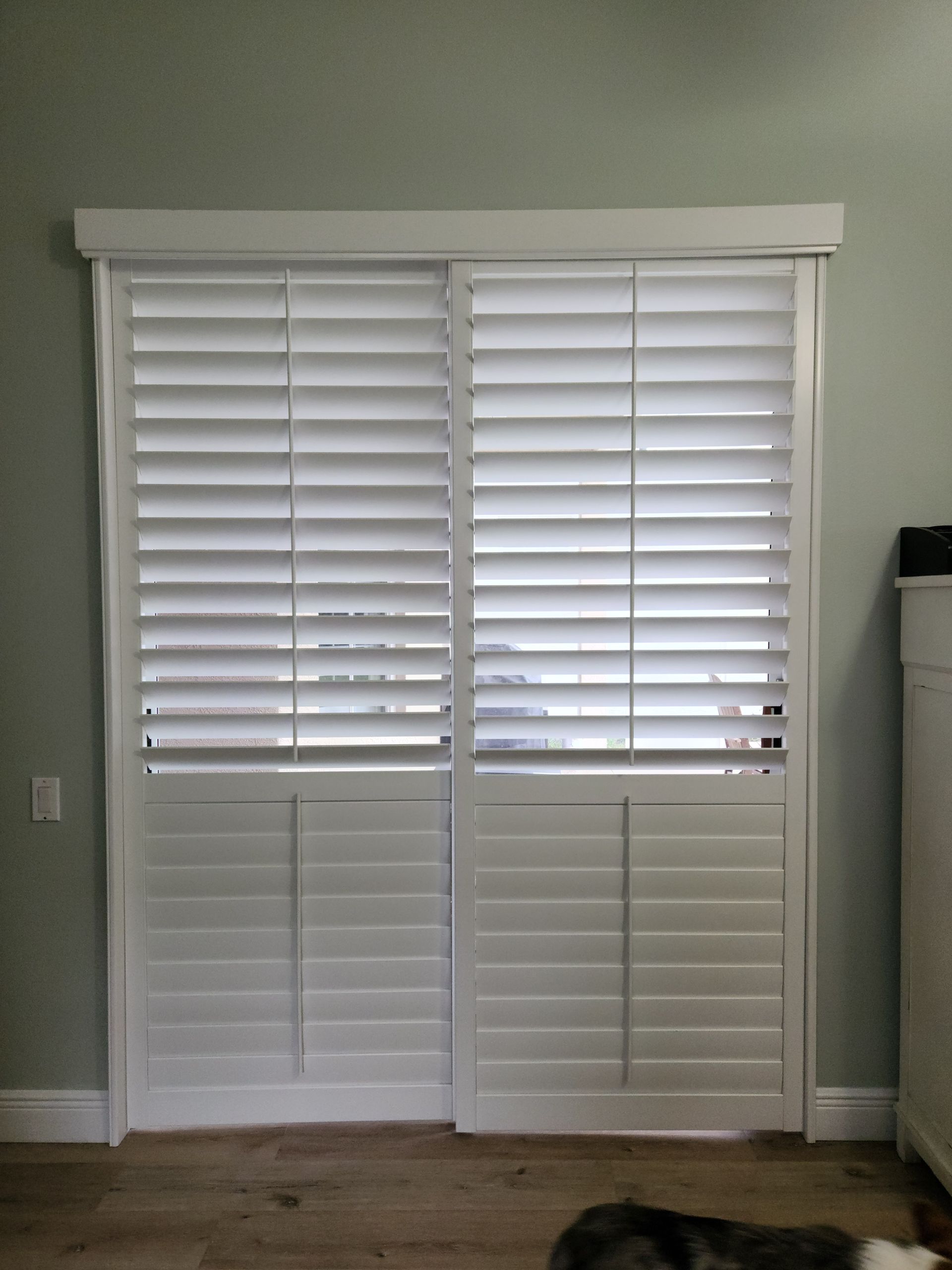 White plantation shutters on a sliding door, closed with slats open, set in a room with light green walls.