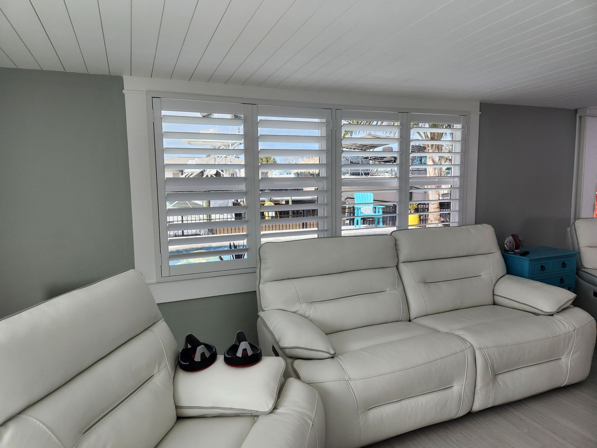 White leather sofa and chair in front of a window with white shutters; gray walls.