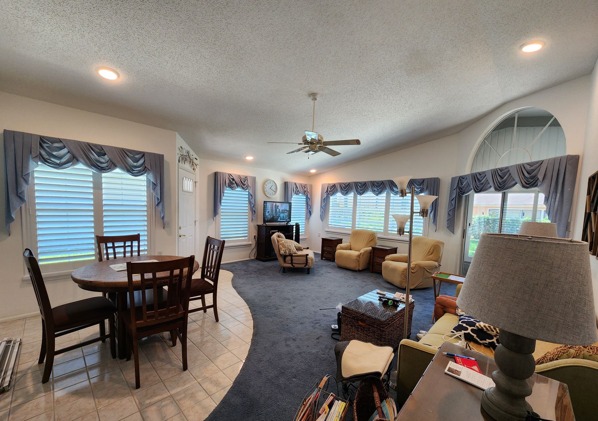 Living room with blue curtains, dark blue rug, dining area, and tan armchairs.