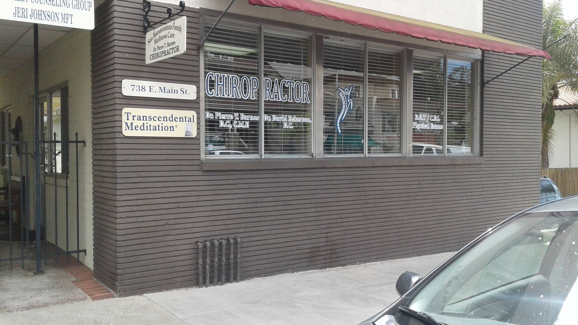Exterior of a dental office with brick facade, large windows, and a red awning.