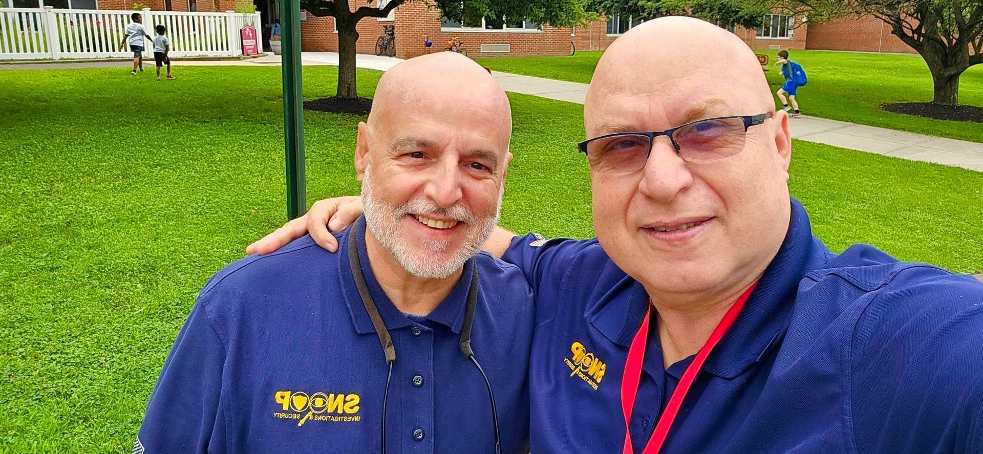 Two men in blue shirts smiling for a selfie in a green park