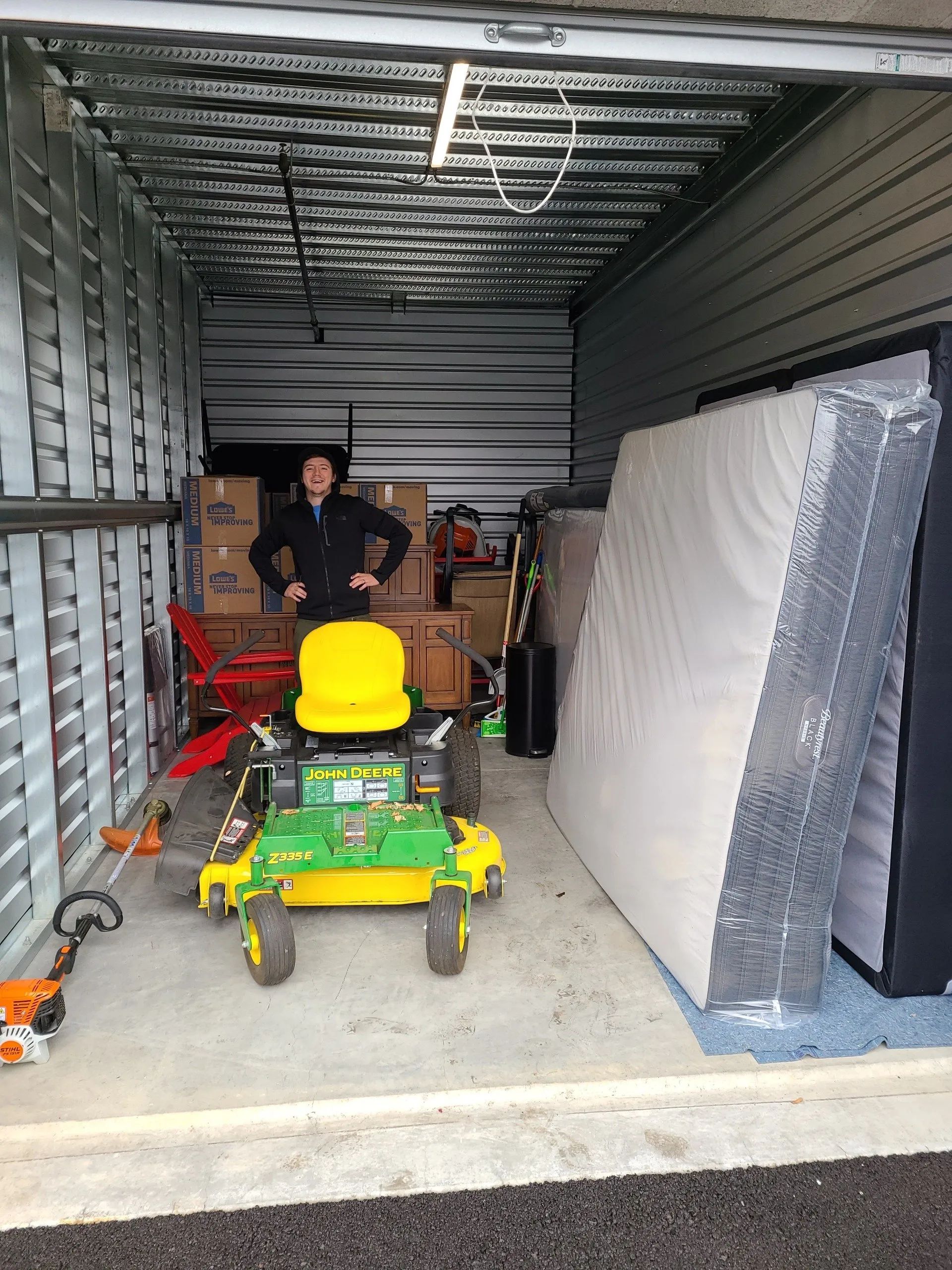 Person in storage container with yellow lawn mower and wrapped mattress inside a trailer