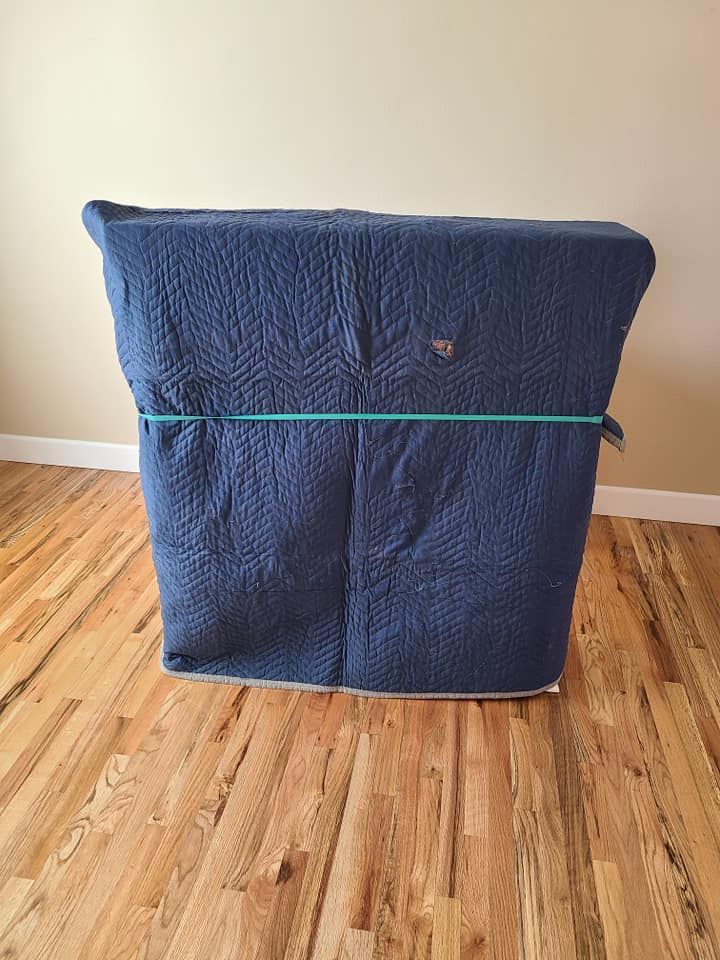 Blue cushioned chair or ottoman strapped with a teal band, sitting on a hardwood floor.
