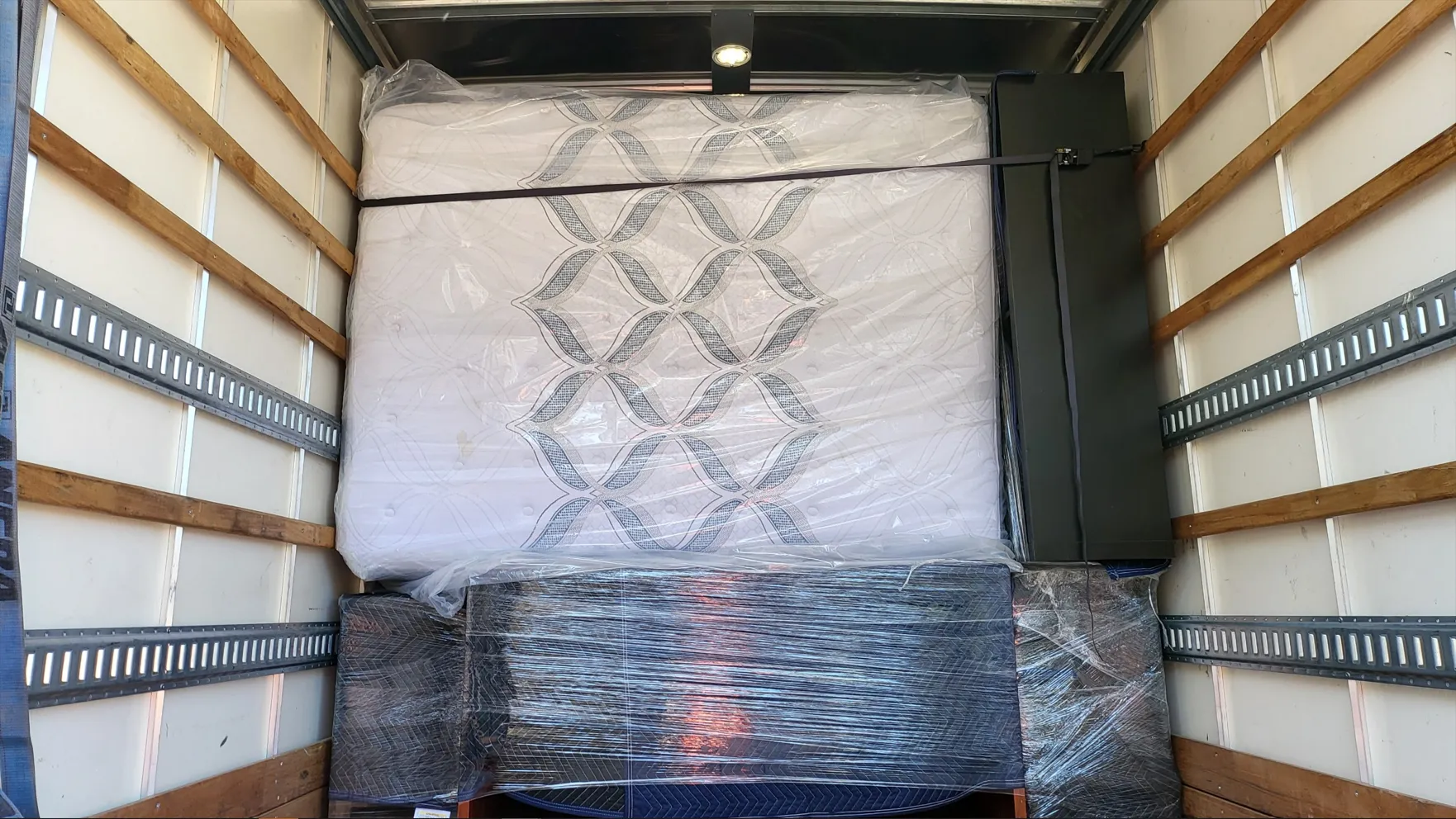 Inside a moving truck, a large wrapped appliance or furniture item is secured against the front wall.