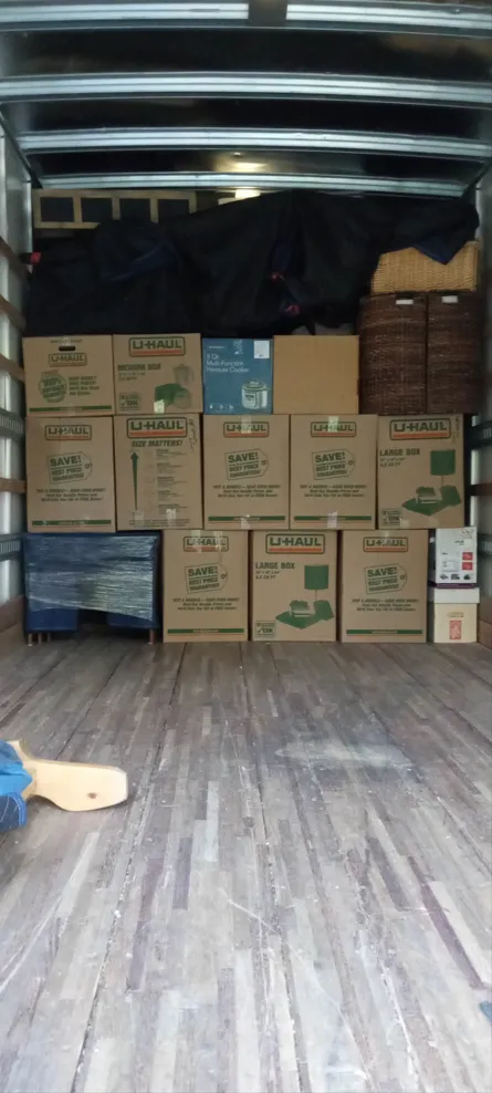 Cargo truck interior packed with stacked cardboard boxes and a black tarp, viewed from the rear door