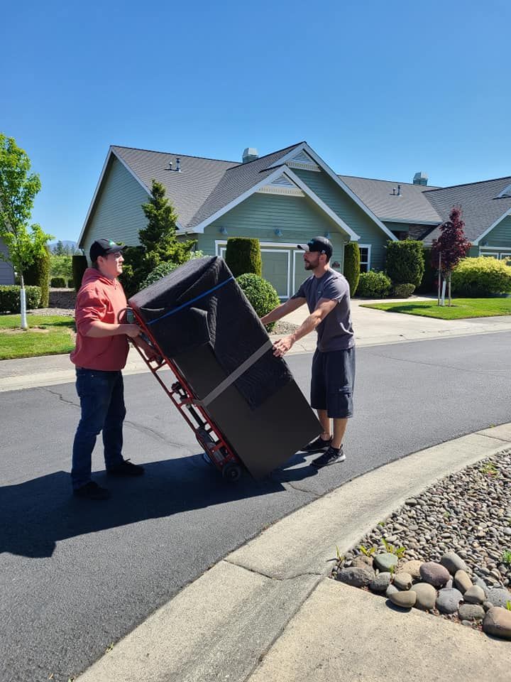 Two people carrying a large black couch on a suburban street near houses.