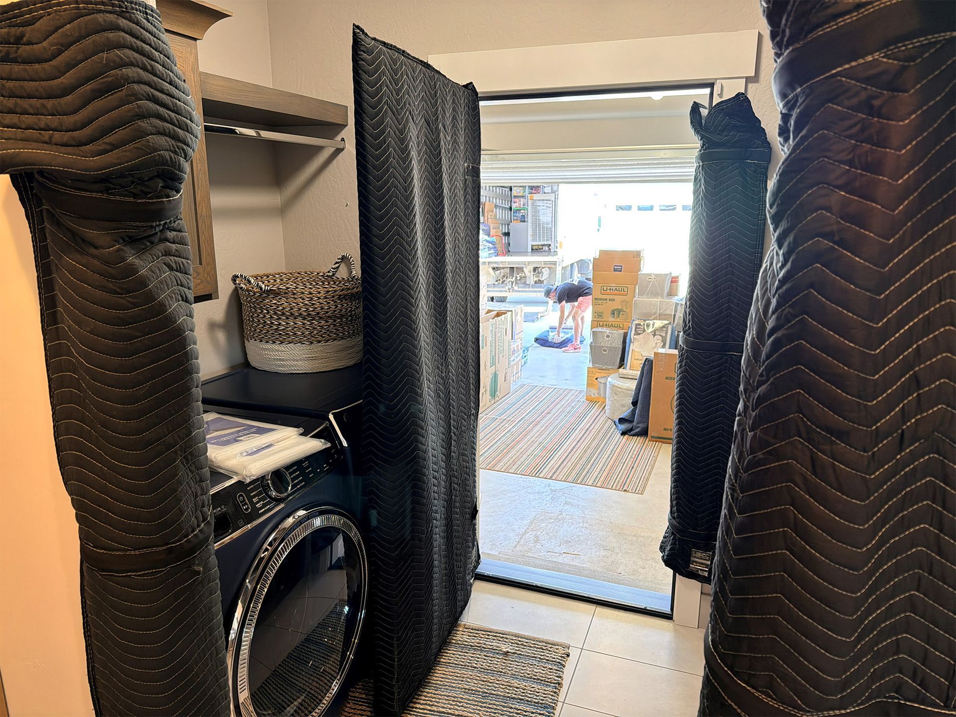 Moving truck viewed through a doorway, with blankets wrapped around furniture and boxes stacked in the hall.