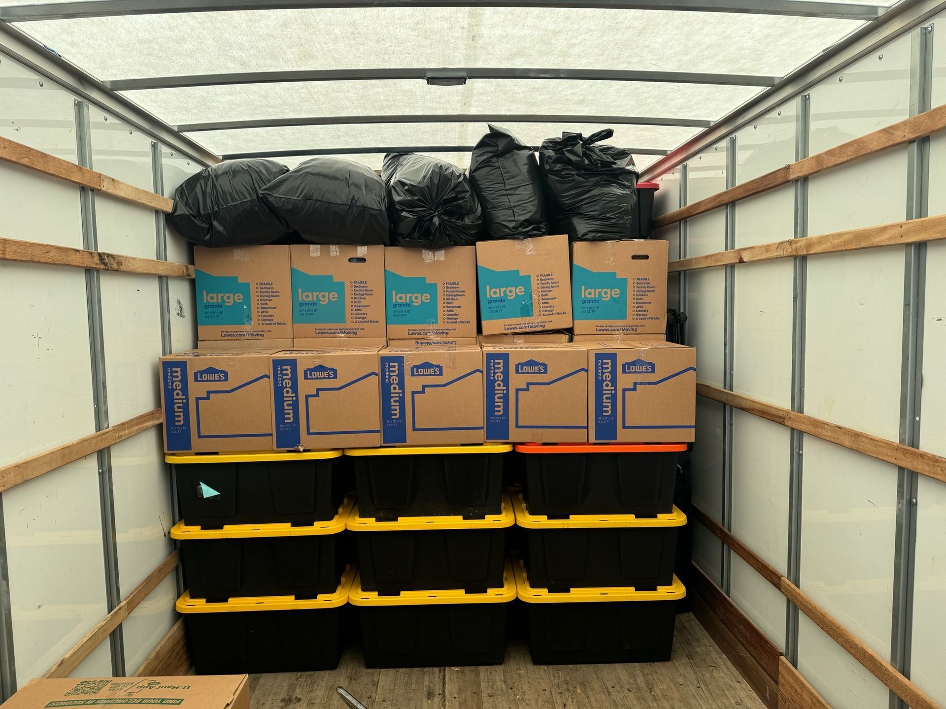 Packed moving truck with stacked cardboard boxes and black bins inside.