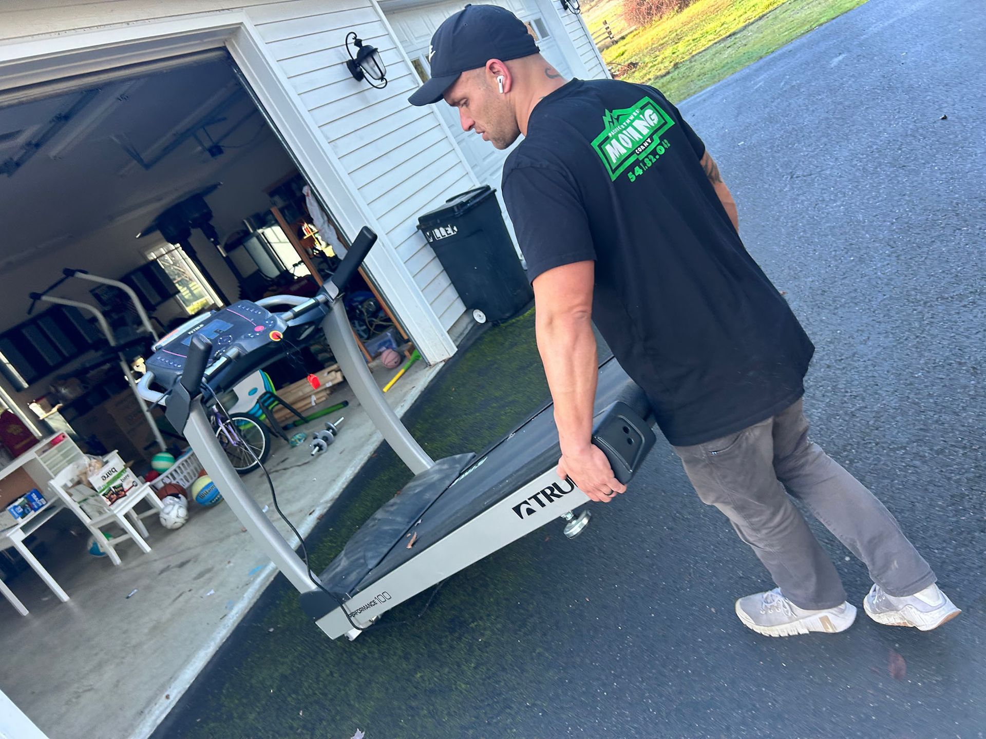 Man in black cap and shirt carries a metal ramp from an open garage to a driveway.
