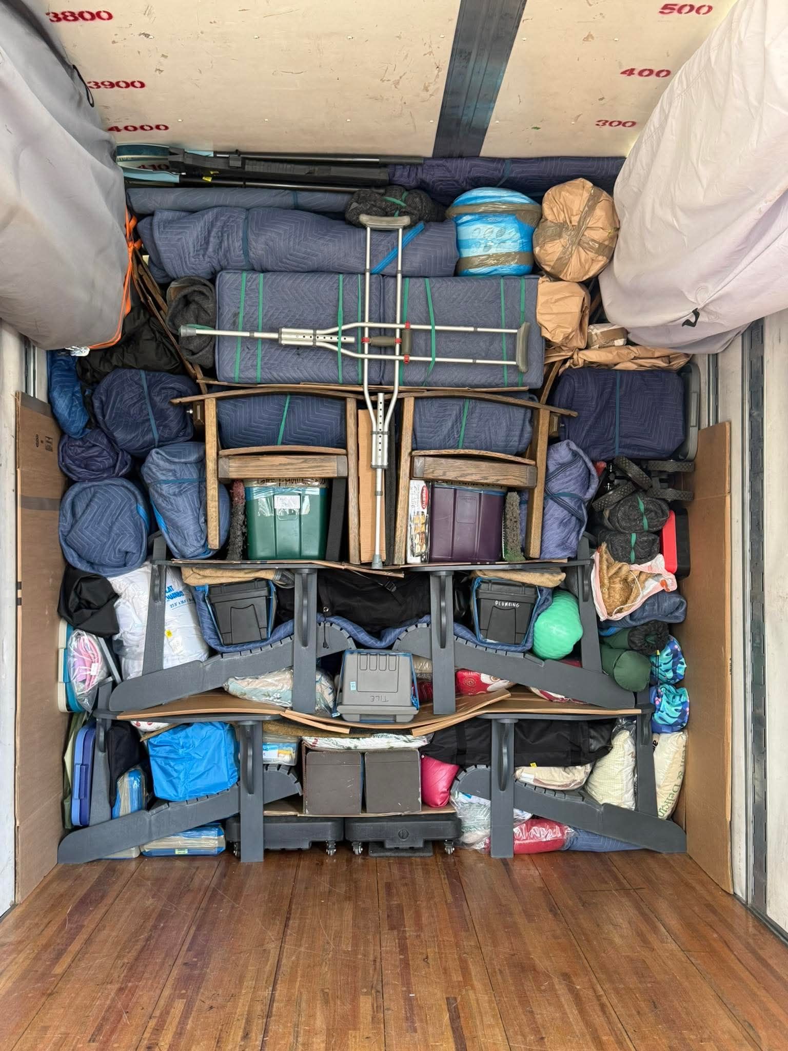 Packed storage area viewed from above, with bins, bags, and strapped cargo in a narrow compartment.