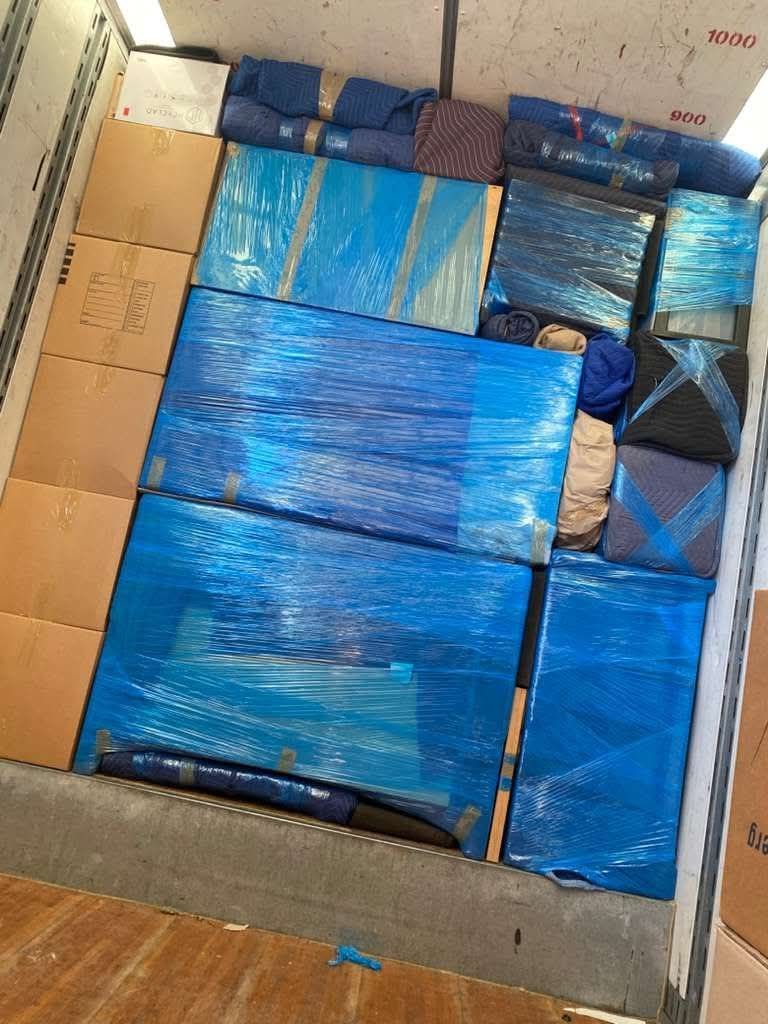 Open cardboard box filled with blue plastic-wrapped packages and packing materials