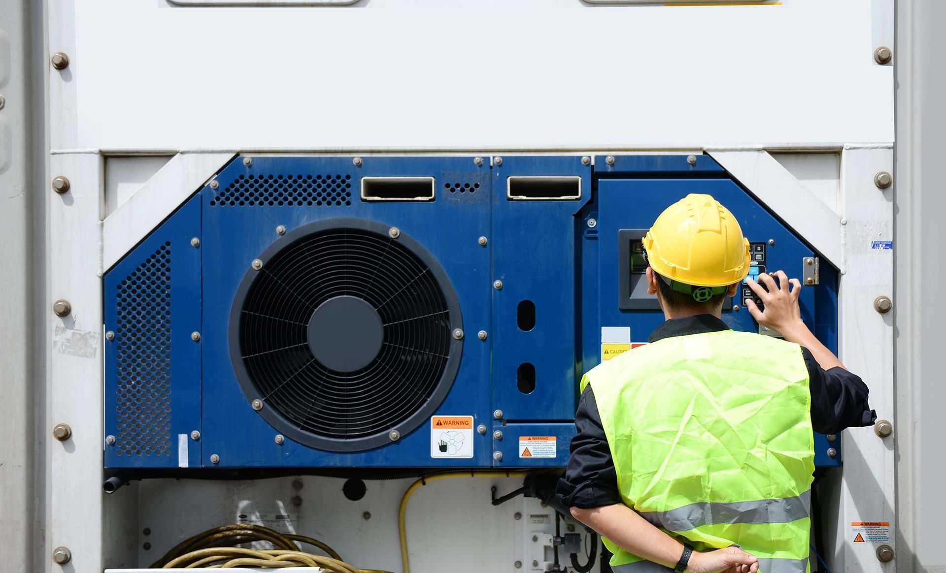 A man in a yellow hard hat is working on a refrigerator.