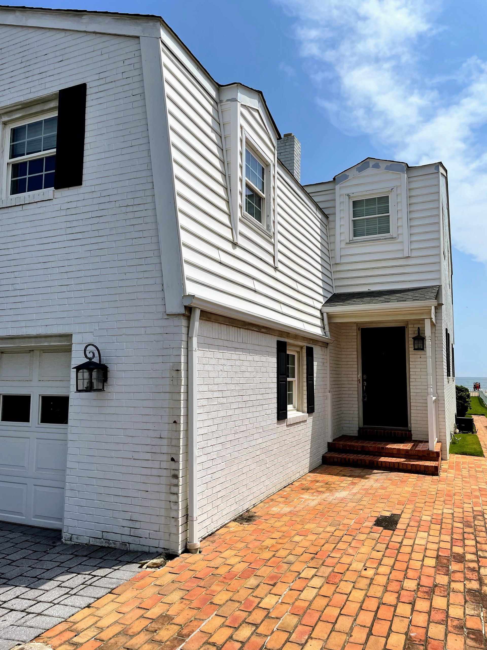 White house with a Dutch gambrel roof, brick walkway, and blue sky.