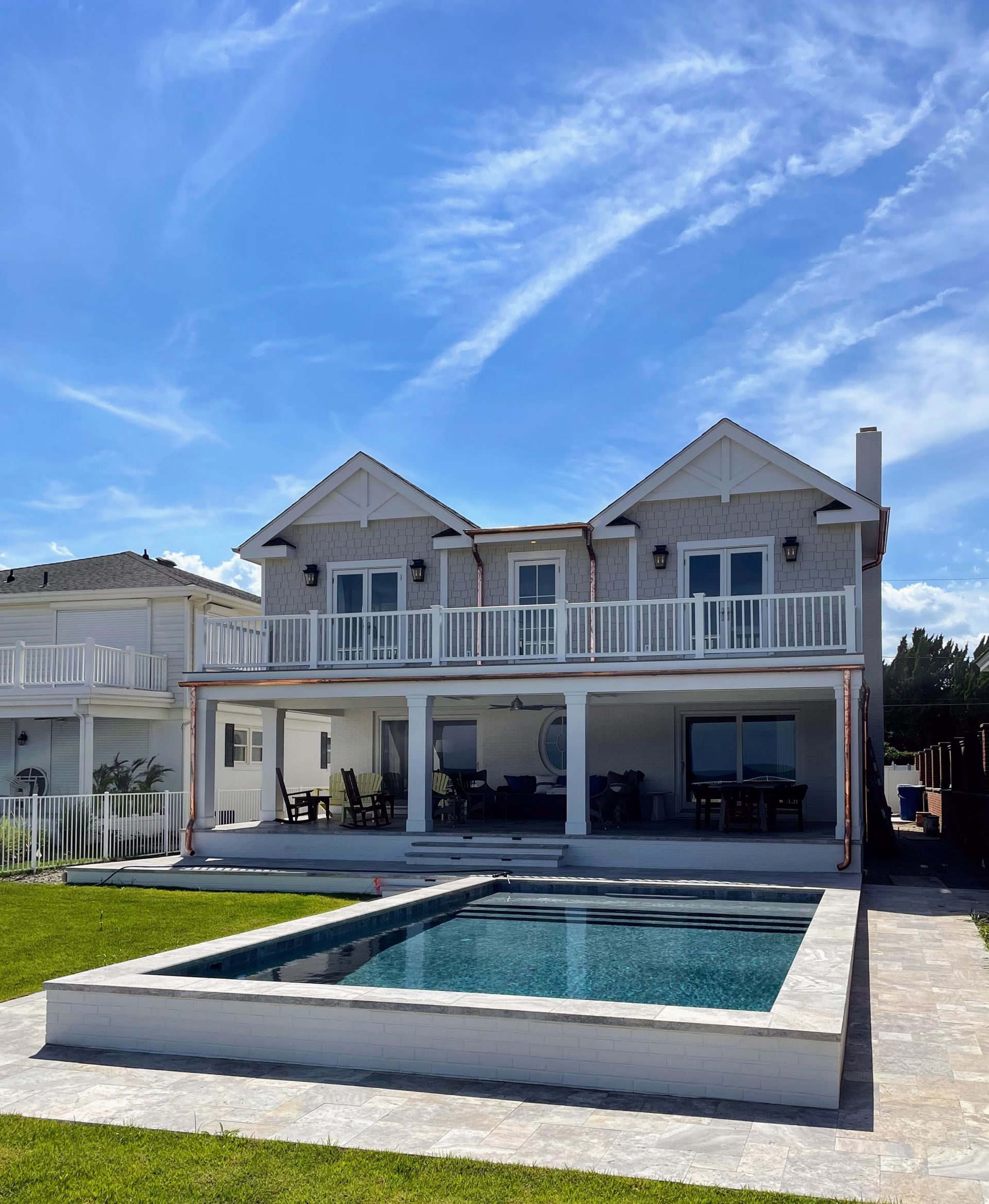 Two-story house with balcony, white trim, and a pool. Blue sky, green grass.