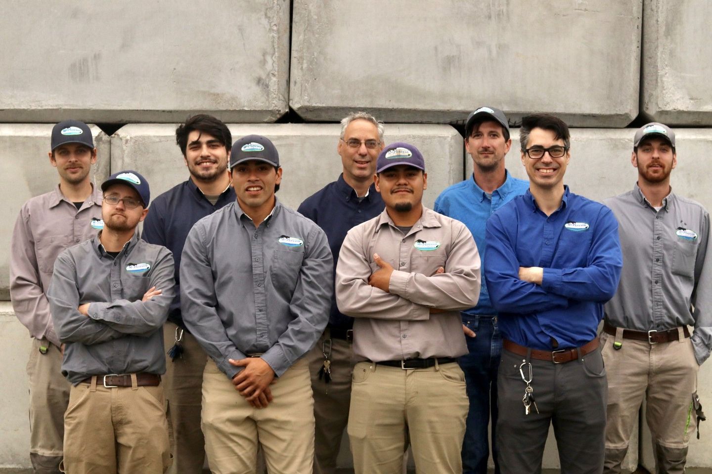 Seven workers standing shoulder to shoulder in gray and blue uniforms against a concrete wall