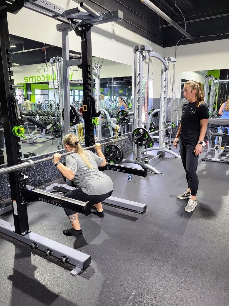 A woman is squatting with a barbell in a gym.