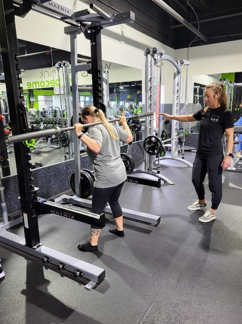 A woman is squatting with a barbell in a gym.