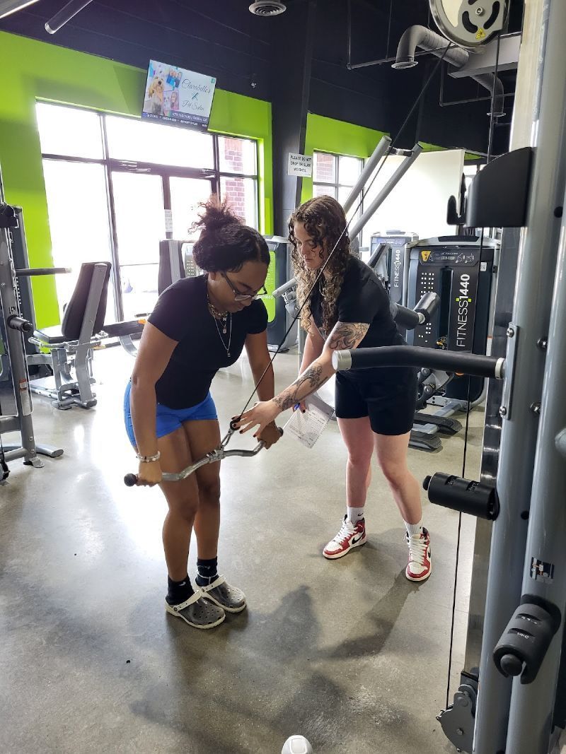 A woman is teaching another woman how to use a machine in a gym.