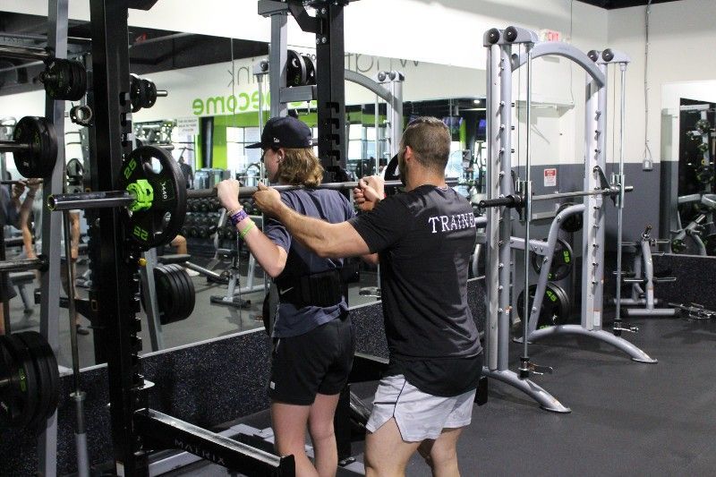 A man is helping a woman squat in a gym.