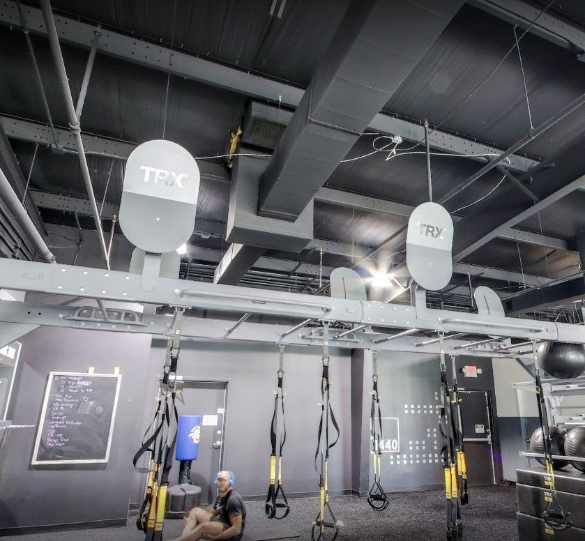 A man sits on the floor in a gym with a trx sign hanging from the ceiling