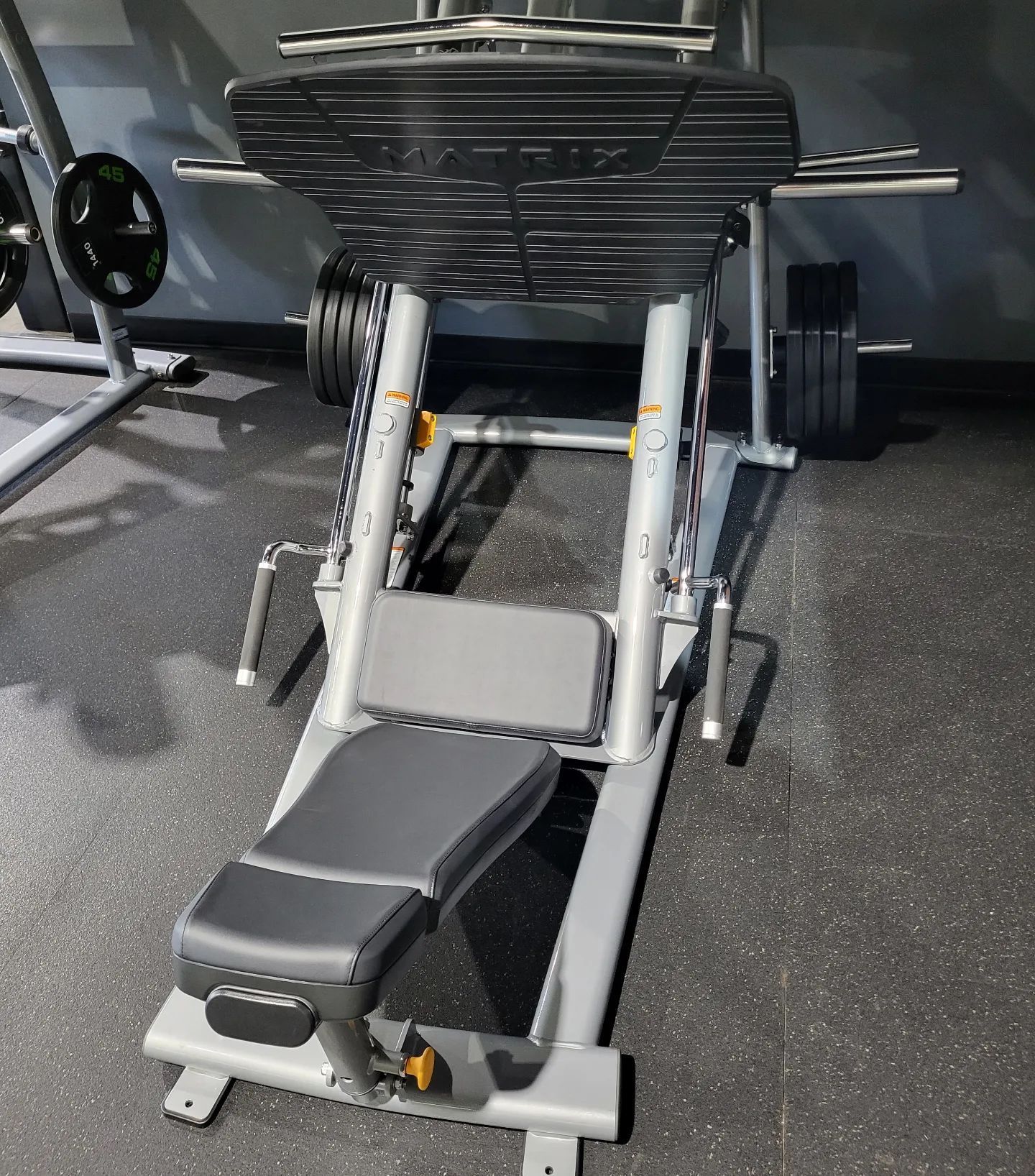 A leg press machine is sitting on the floor in a gym.