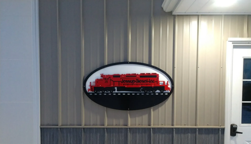 Oval wall sign with red text on a beige paneled building beside a white door