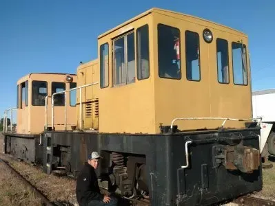 Yellow railroad maintenance vehicle on tracks with a worker standing beside it under a blue sky