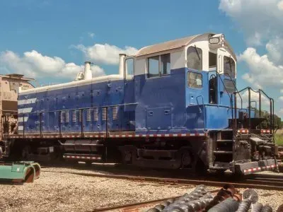 Blue locomotive on display outdoors under a cloudy sky, with tracks and gravel in the foreground