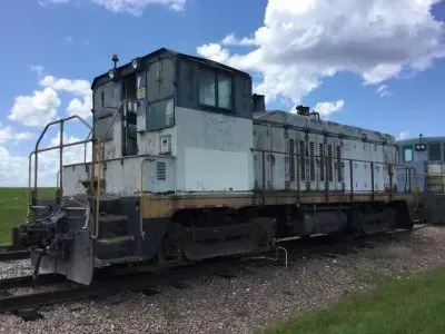 White and blue diesel locomotive on tracks under a cloudy sky at a rail yard