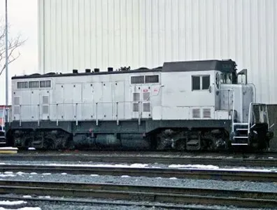 White diesel locomotive on tracks beside a large building on a snowy day