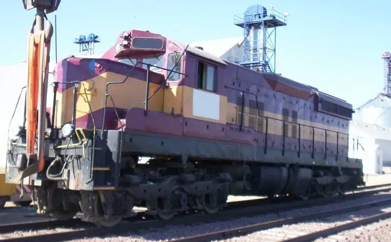 Yellow and maroon locomotive parked on train tracks beside a station platform under a clear sky