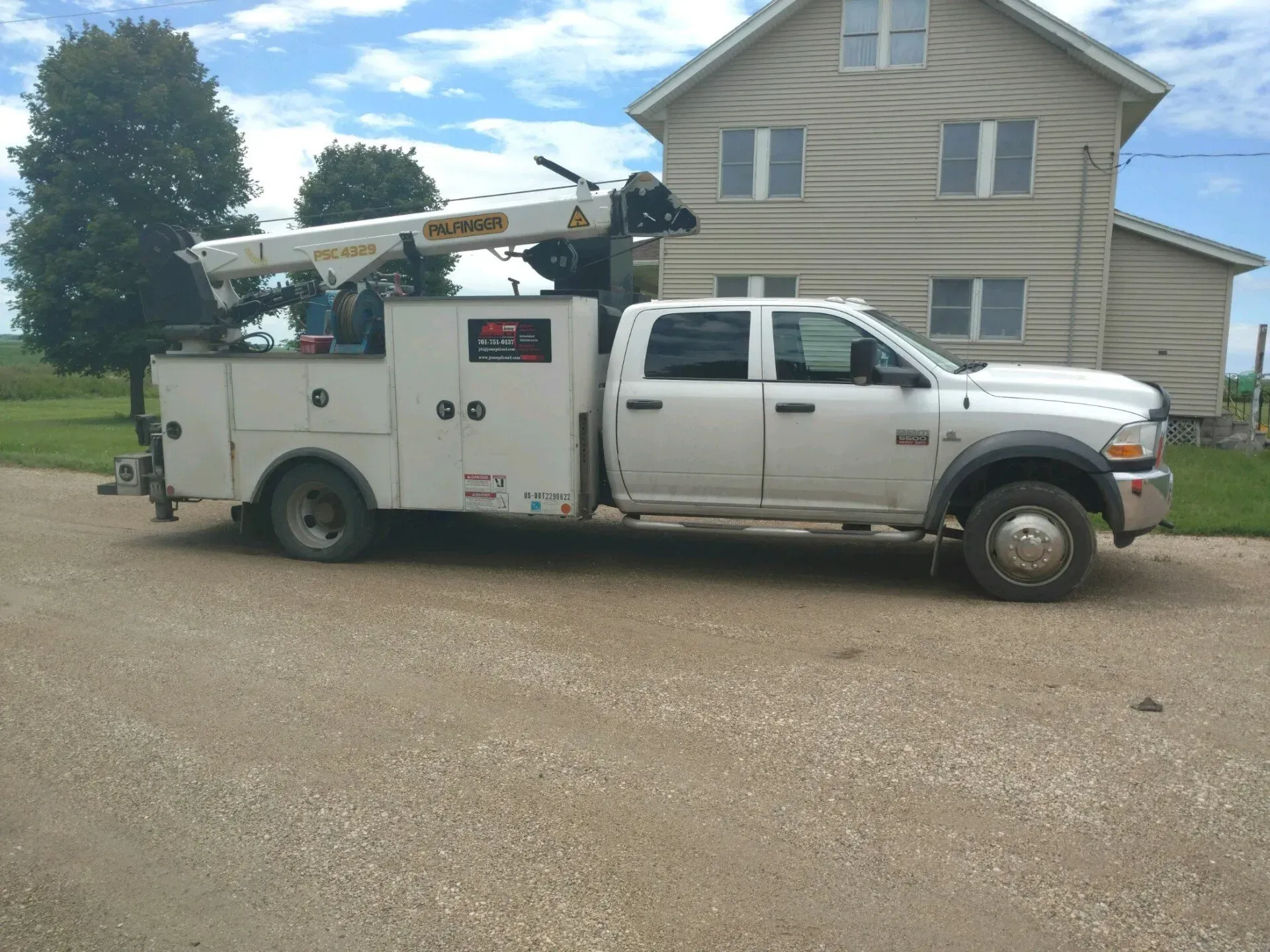 White utility truck with bucket lift parked on gravel in front of a house
