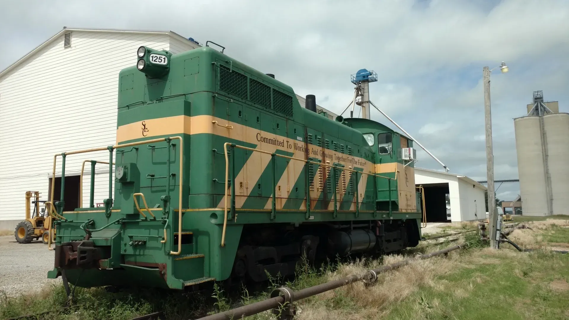 Green and yellow locomotive parked beside a white industrial building under a clear sky