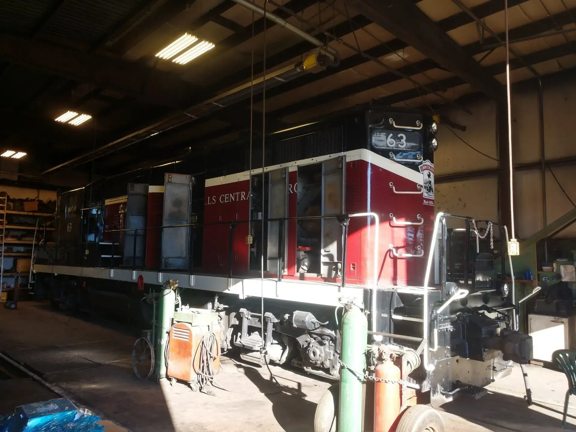 Red locomotive inside a rail maintenance shed with bright overhead lights.