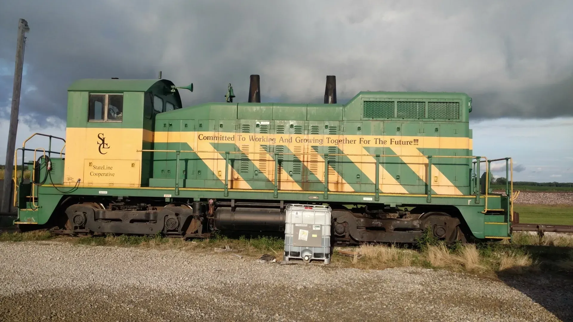 Green and yellow locomotive on tracks under cloudy sky in a grassy field